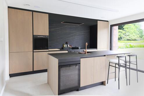 Tijdloze maatkeuken Izegem met kookeiland, eiken fineer, keramisch werkblad Noir Desir en zitplaatsen aan het eiland.